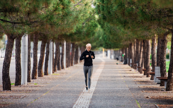 A front view of young sportswoman running outdoors in park.