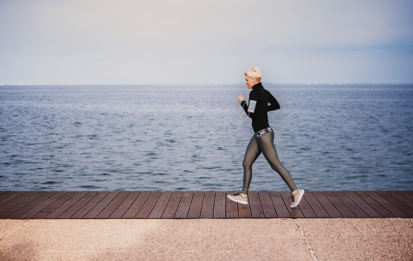 Side view of young sportswoman running outdoors on beach. Copy space.