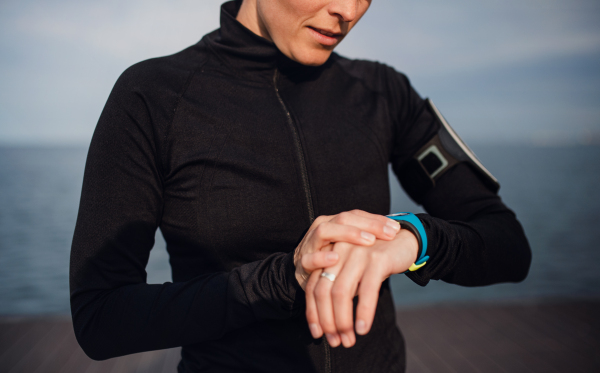 A midsection of young sportswoman standing outdoors on beach, using smartwatch.