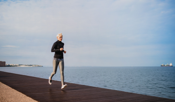 Side view of young sportswoman running outdoors on beach. Copy space.