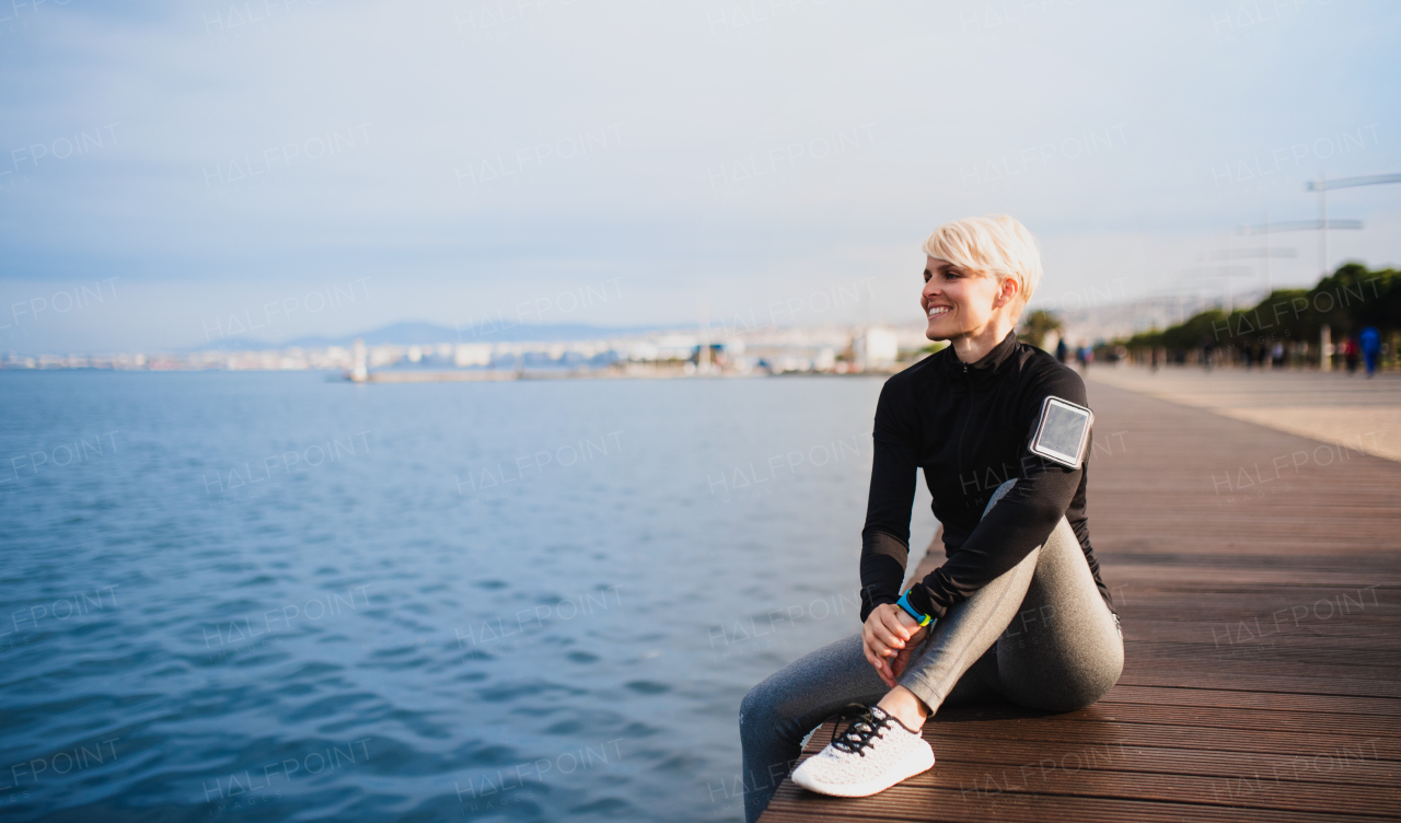 A portrait of young sportswoman sitting outdoors on beach. Copy space.