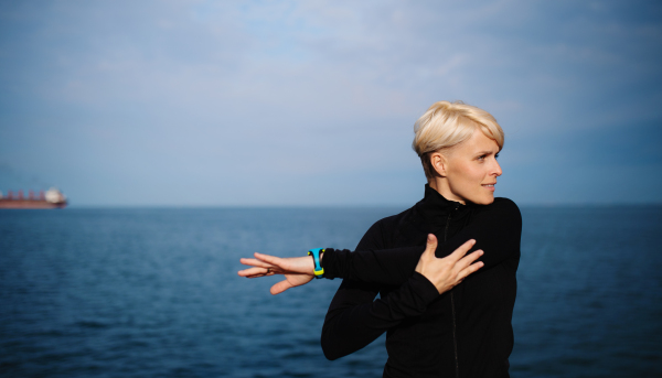 Front view portrait of young sportswoman sitting outdoors on beach, stretching. Copy space.