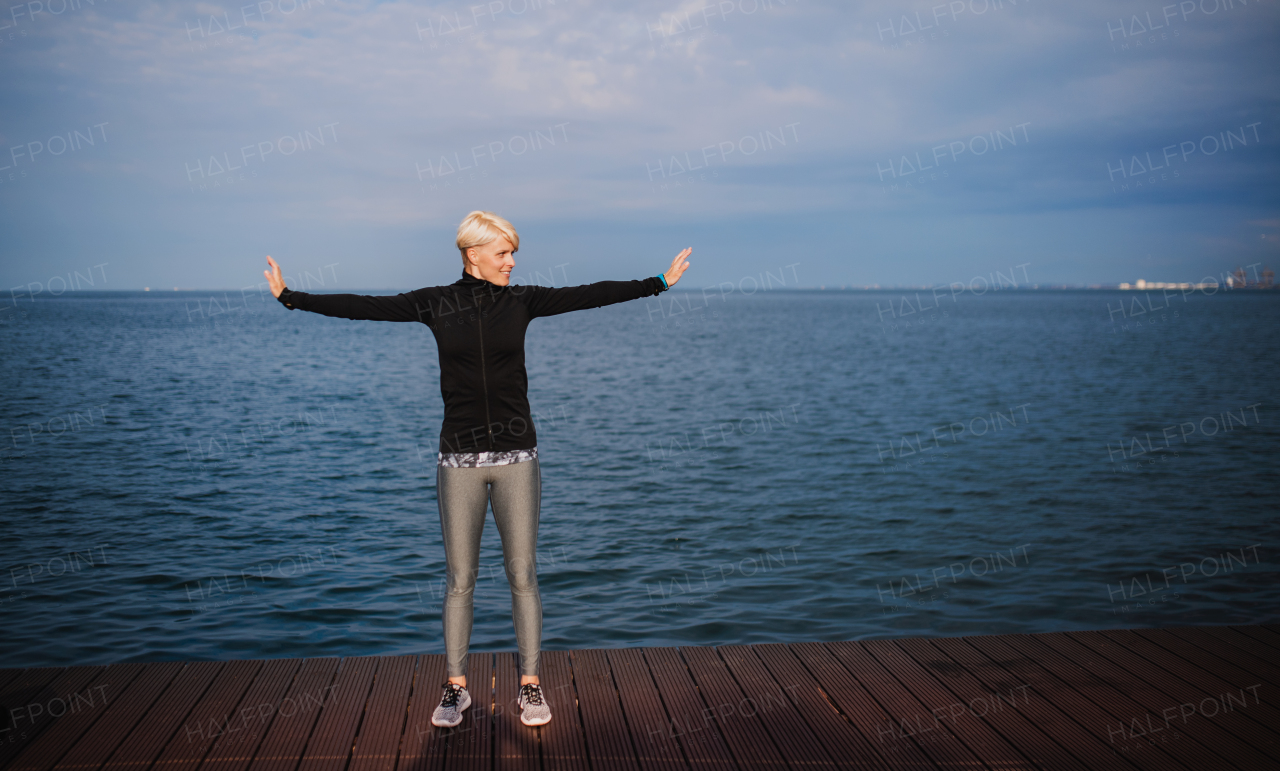 Side view portrait of young sportswoman standing outdoors on beach, stretching. Copy space.