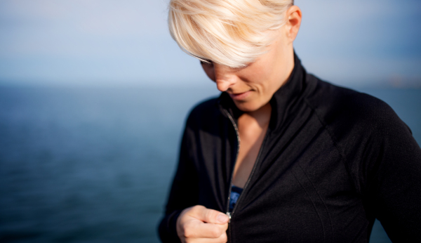 Midsection of young sportswoman standing outdoors on beach, close-up.