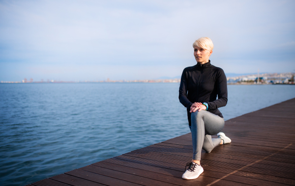 A portrait of young sportswoman standing outdoors on beach, stretching. Copy space.