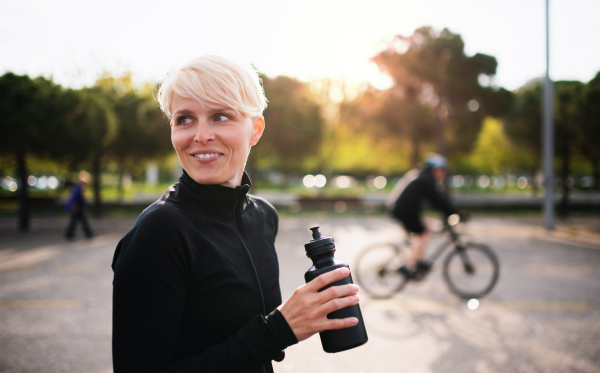 Portrait of young sportswoman standing outdoors in town, holding water bottle. Copy space.