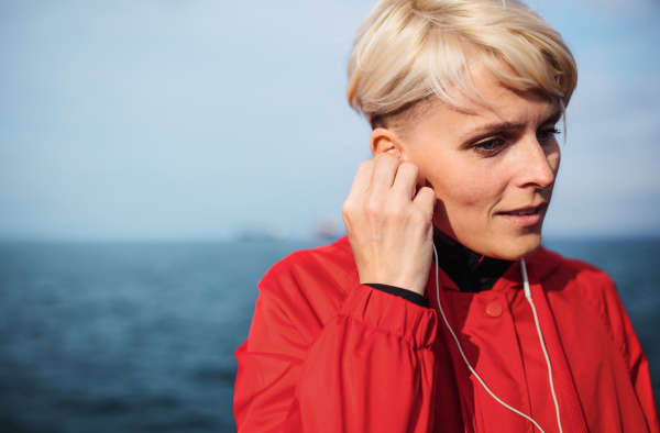 Front view portrait of young sportswoman with earphones standing outdoors on beach.