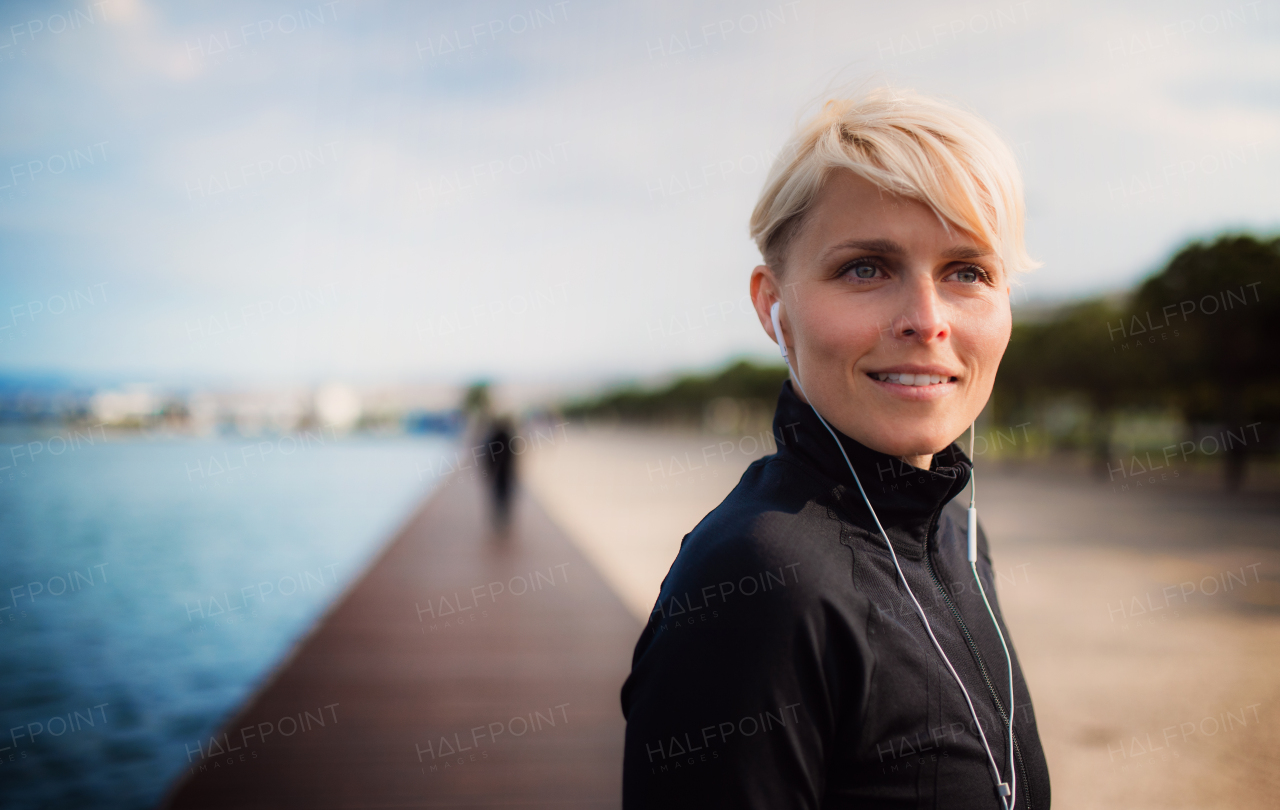 A portrait of young sportswoman with earphones standing outdoors on beach. Copy space.