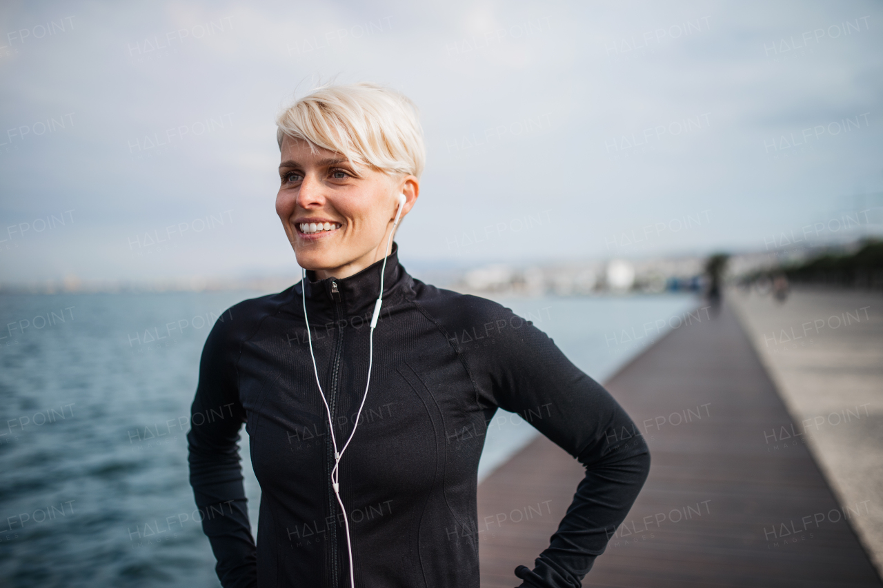 Front view portrait of young sportswoman with earphones standing outdoors on beach.