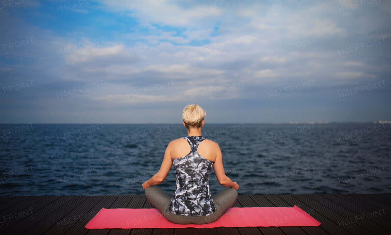 Rear view of young sportswoman doing yoga exercise on beach. Copy space.