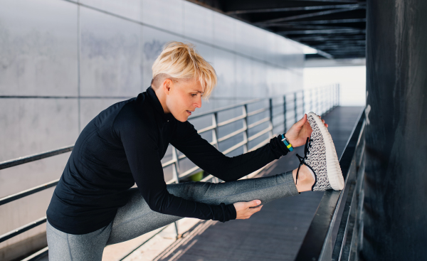 A portrait of young sportswoman with earphones doing exercise outdoors, stretching.