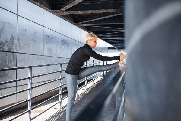 A portrait of young sportswoman with earphones doing exercise outdoors, stretching.