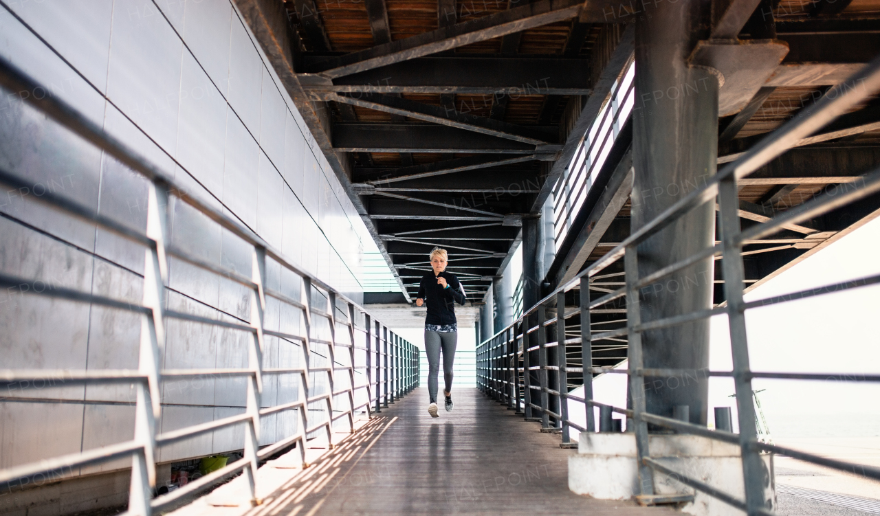 A young sportswoman doing exercise outdoors under bridge, running.