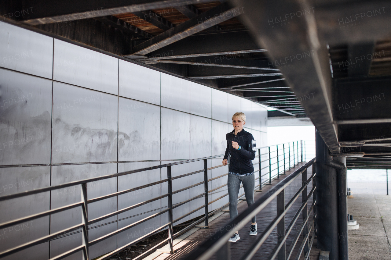 A young sportswoman doing exercise outdoors under bridge, running.