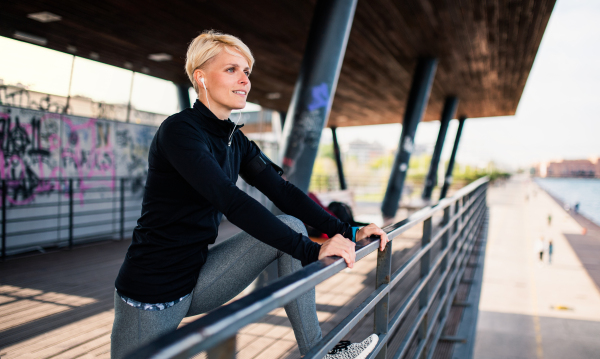 A young sportswoman with earphones doing exercise by sea, stretching.