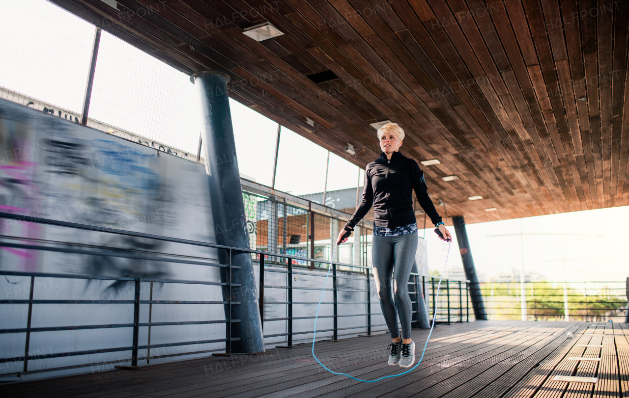 A fit young sportswoman doing exercise outdoors, skipping.