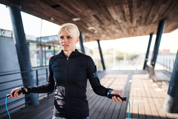 A fit young sportswoman doing exercise outdoors, skipping.