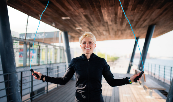 A fit young sportswoman doing exercise outdoors, skipping.