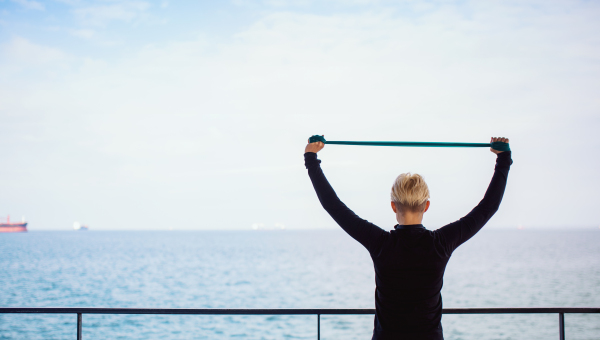 A rear view of young sportswoman doing exercise with elastic bands by sea. Copy space.