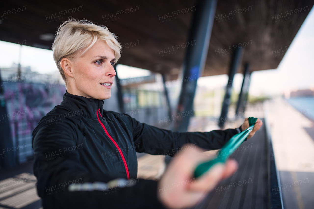 A young sportswoman with elastic band doing exercise outdoors in city. Copy space.