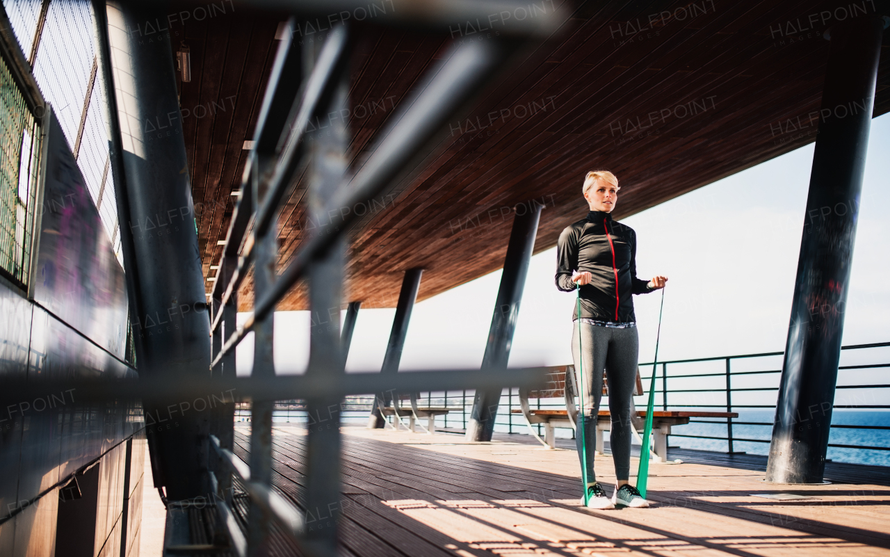 A young sportswoman doing exercise with elastic bands by sea.