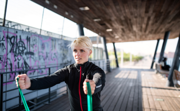 A young sportswoman with elastic bands doing exercise outdoors in city. Copy space.