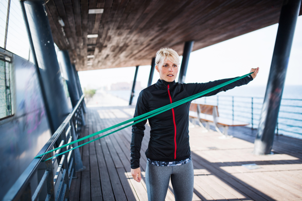 A young sportswoman with elastic band doing exercise outdoors in city. Copy space.