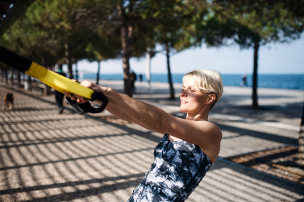 An attractive young sportswoman doing exercise with TRX fitness straps outdoors.