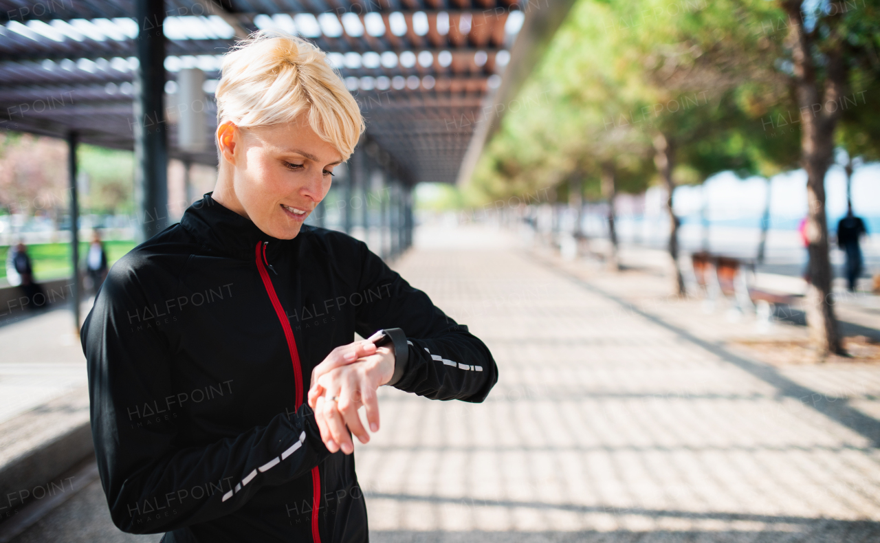 A portrait of young sportswoman with smartwatch resting after doing exercise outdoors. Copy space.