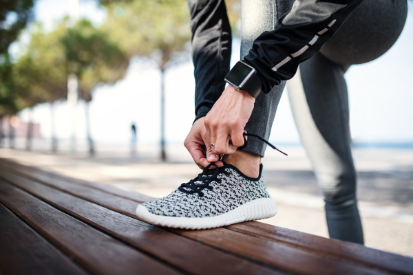 A midsection of young sportswoman with smartwatch outdoors in city, tying shoelaces.