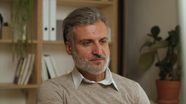 A portrait of businessman sitting at the desk indoors in office, working.