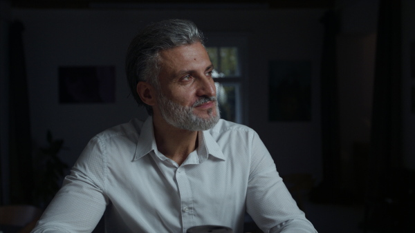 A portrait of businessman sitting at the desk indoors in office, working late.