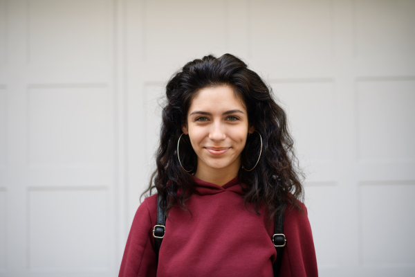 Portrait of happy young woman standing outdoors against white background, looking at camera.