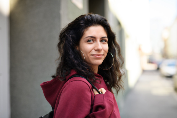 A portrait of young woman standing outdoors on street in city.