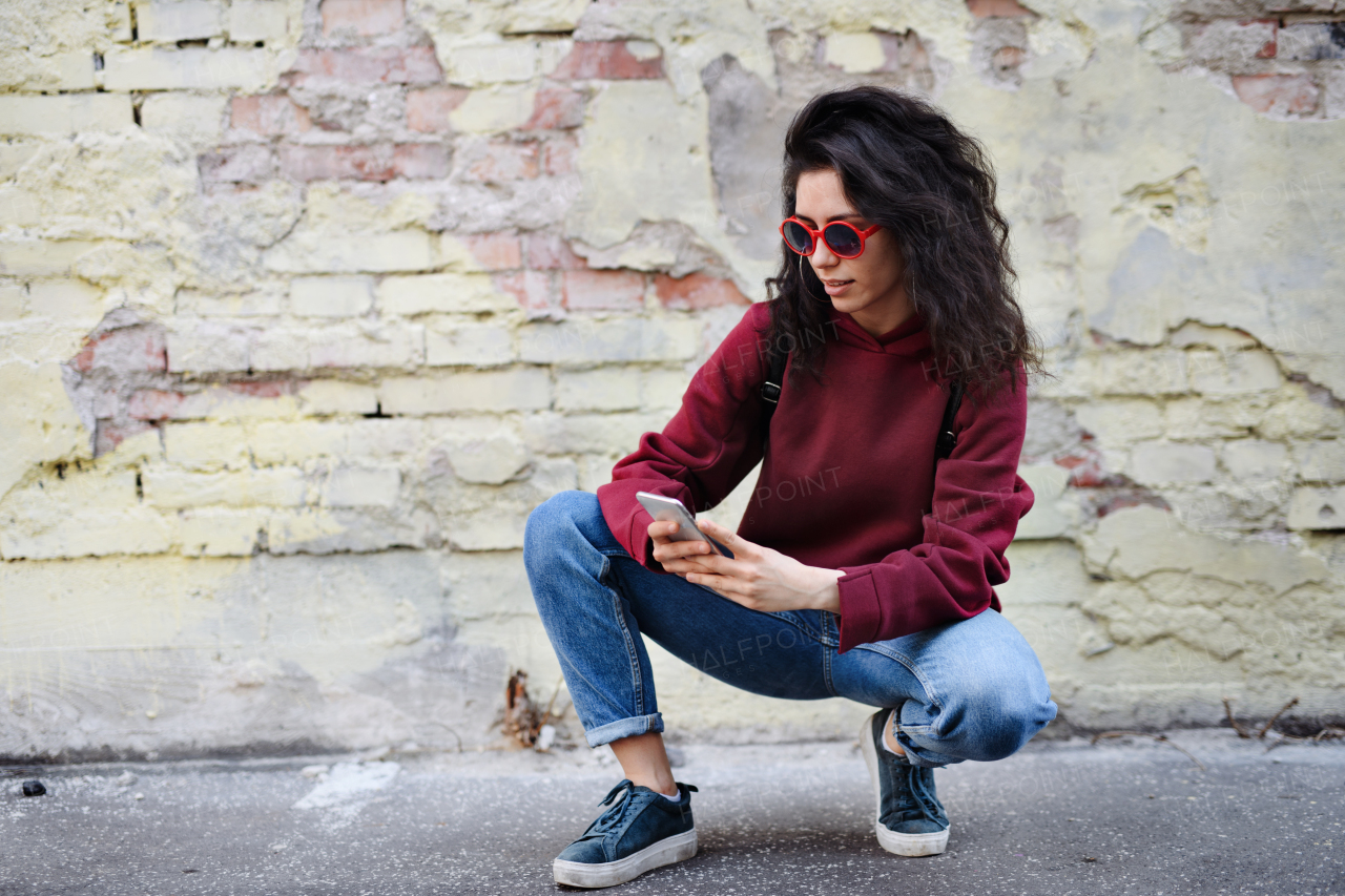 A portrait of young woman standing outdoors on street in city, using smartphone.