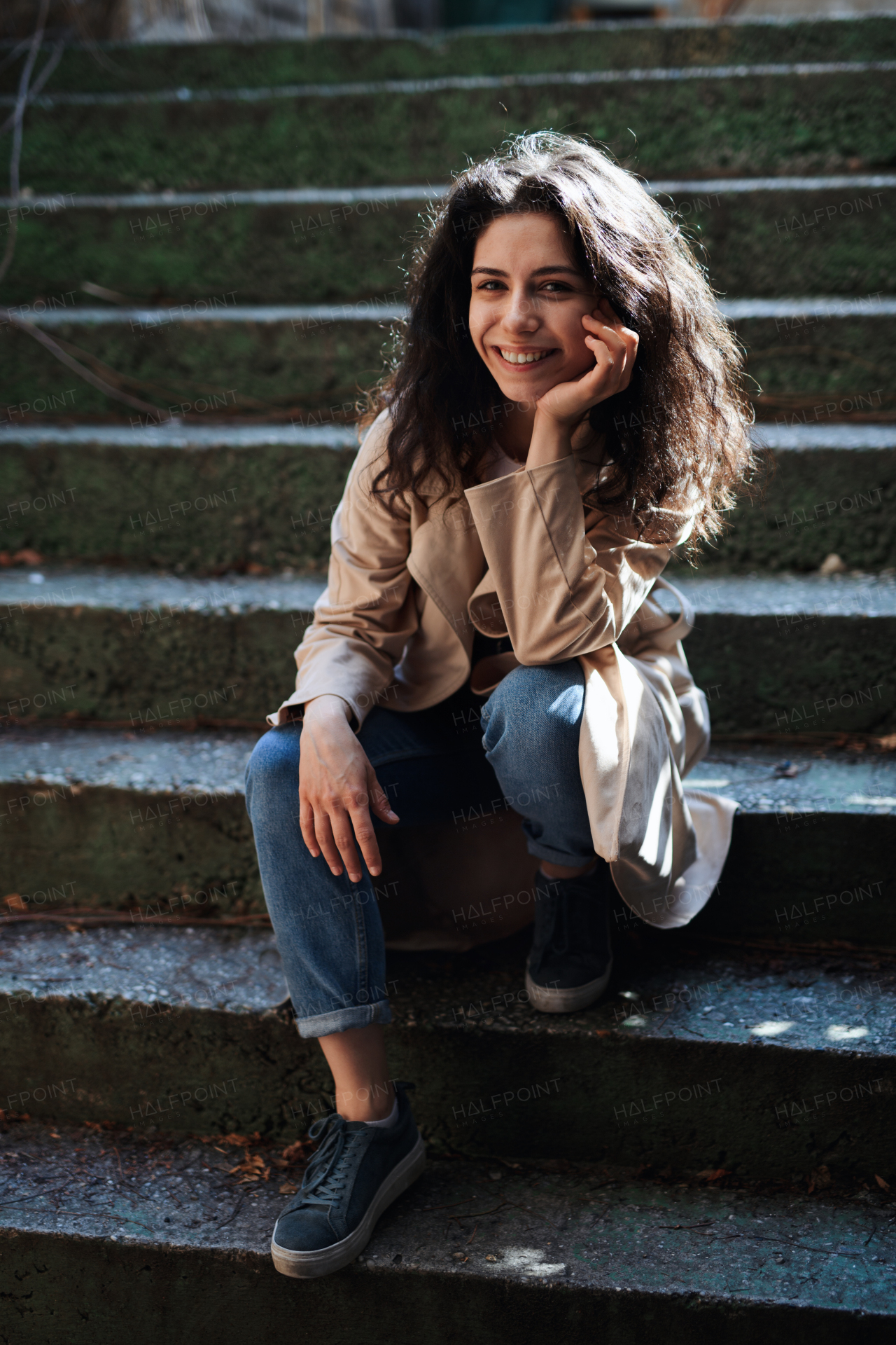 A front view portrait of young woman sitting on staircase outdoors on street in city, looking at camera.