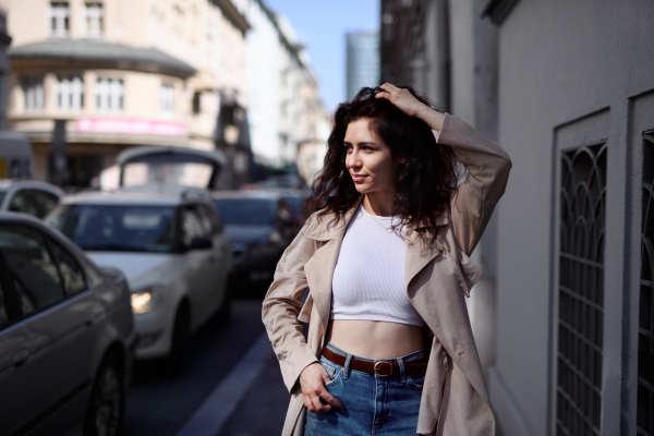 A front view portrait of young woman walking outdoors on street in city.