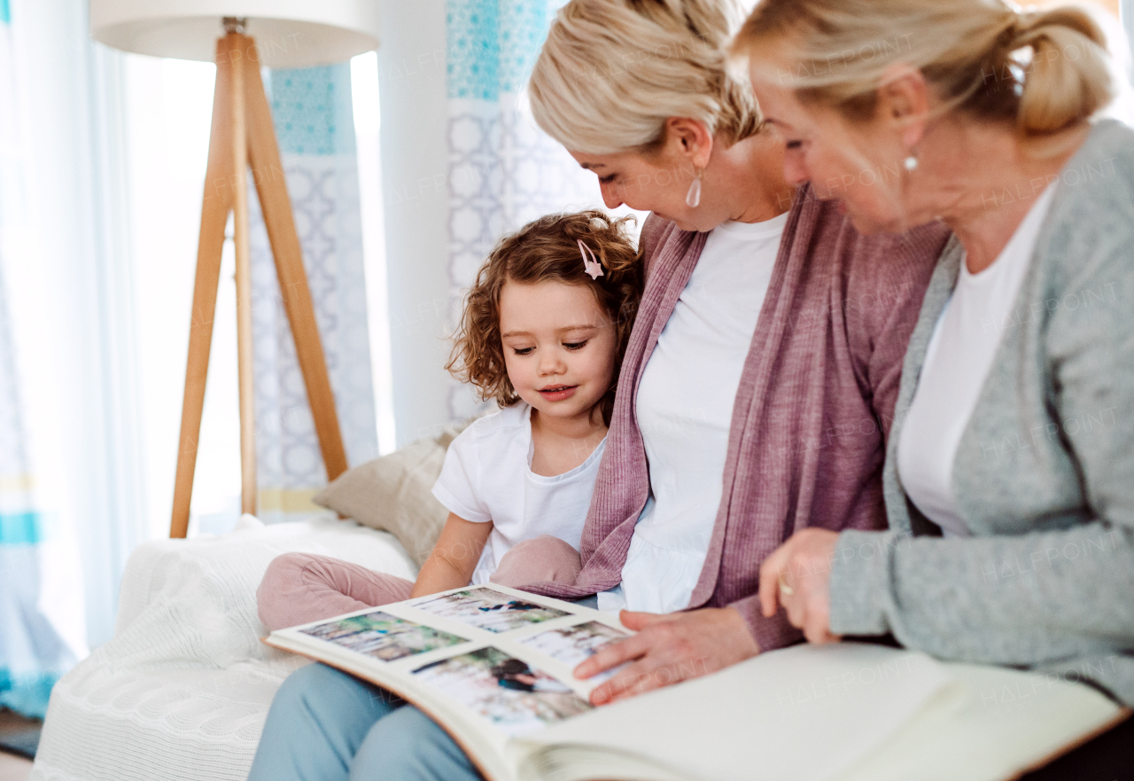 A small girl with mother and grandmother sitting on a sofa at home, looking at photographs.