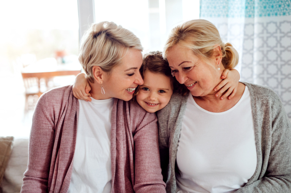 A portrait of happy small girl with mother and grandmother at home, hugging.