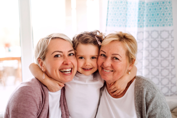 A portrait of happy small girl with mother and grandmother at home, hugging.