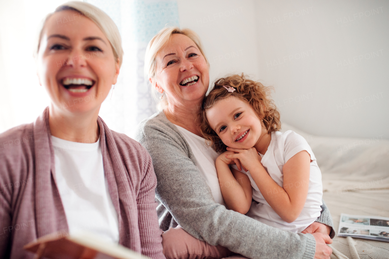 A small girl with mother and grandmother sitting on a sofa at home, laughing.