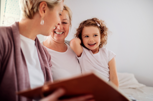 A small girl with mother and grandmother sitting on a sofa at home, looking at photographs.