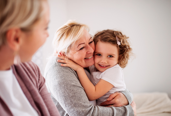 A portrait of happy small girl with mother and grandmother at home, looking at camera.