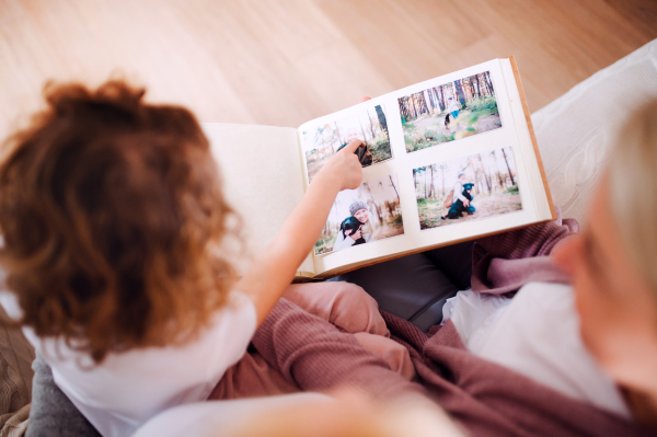 A small girl with mother and grandmother sitting on a sofa at home, looking at photographs. A top view.