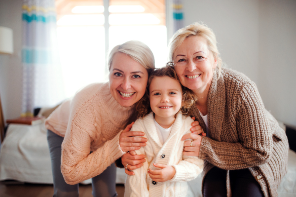 A portrait of happy small girl with mother and grandmother at home, looking at camera.