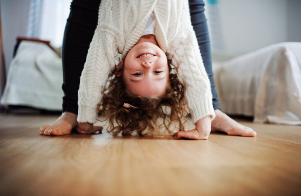 An unrecognizable mother or grandmother holding small girl upside down at home. Copy space.