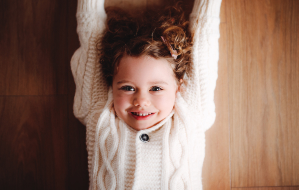 A close-up portrait of happy small girl with white knitted sweater lying on the floor, a top view.