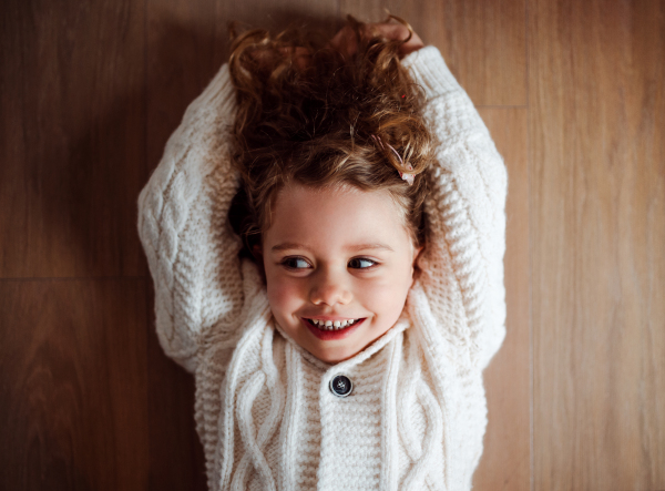 A portrait of happy small girl with white knitted sweater lying on the floor, a top view.