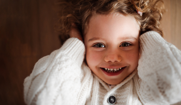 A close-up portrait of happy small girl with white knitted sweater lying on the floor, a top view.