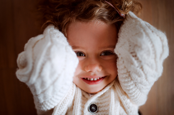 A close-up portrait of happy small girl with white knitted sweater lying on the floor, a top view.